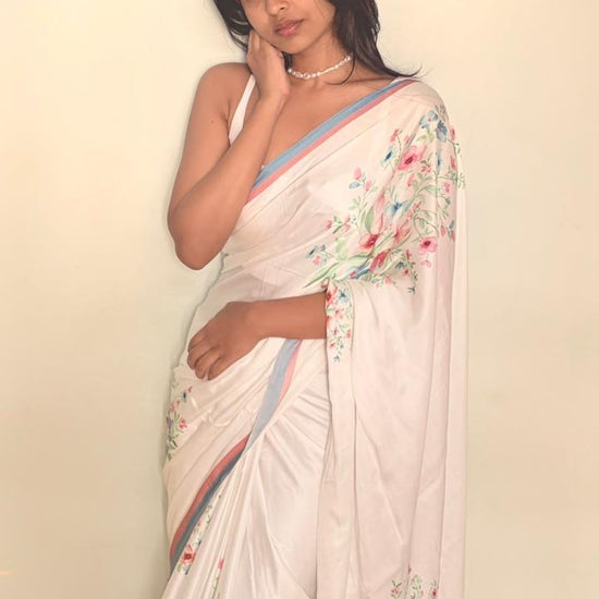 Woman wearing a white saree with floral patterns against a plain background