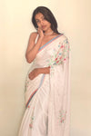 Woman wearing a white saree with floral patterns against a plain background