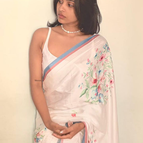 Woman wearing a white saree with floral patterns on a plain background