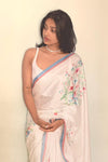 Woman wearing a white saree with floral patterns on a plain background