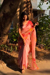 Woman in a pink saree standing outdoors near a tree