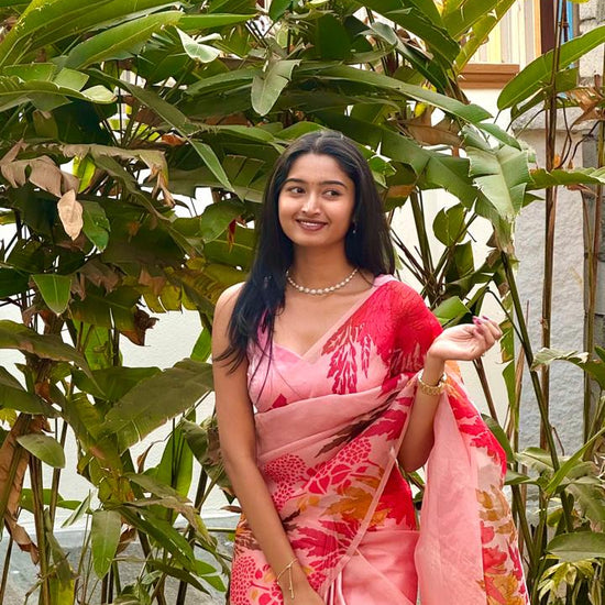 Woman in a pink saree standing among green plants