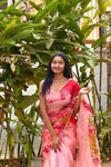 Woman in a pink saree standing among green plants