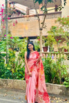 Woman in a pink saree standing in a garden with greenery and flowers around.